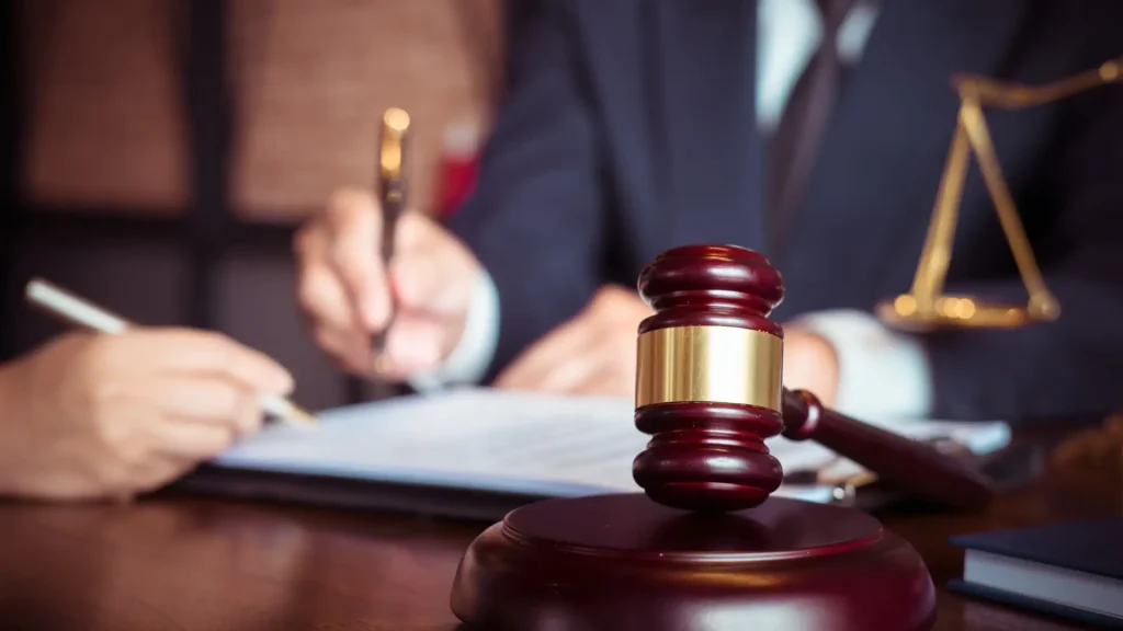 Close-up of a judge's gavel with a person signing legal documents in the background.