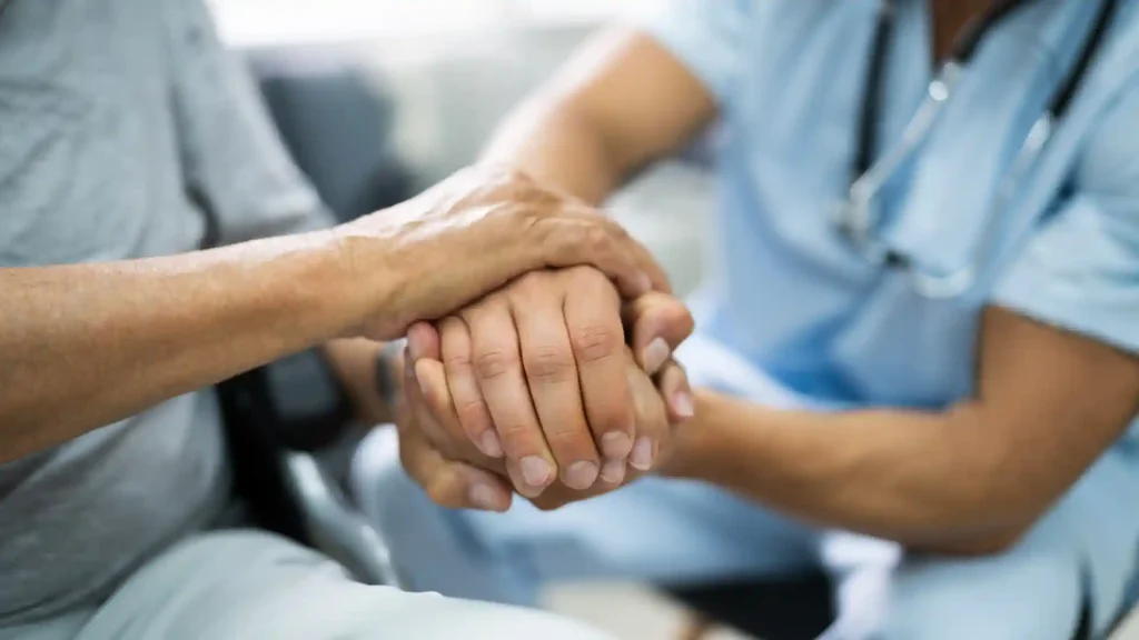 Healthcare worker holding hands with an elderly patient in support.