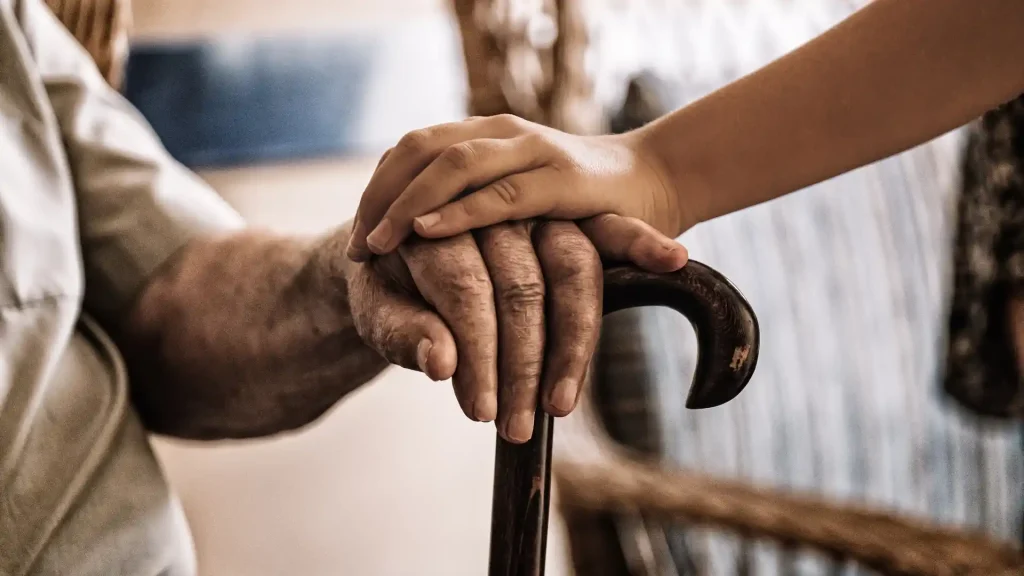 Young hand gently holding an elderly hand resting on a cane